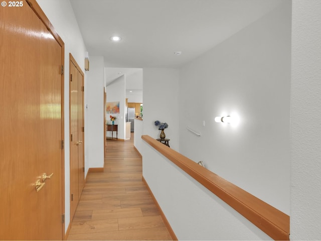 hall featuring light wood-style floors, recessed lighting, baseboards, and an upstairs landing