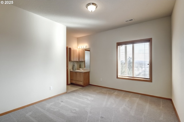 spare room with visible vents, a sink, a textured ceiling, baseboards, and light colored carpet