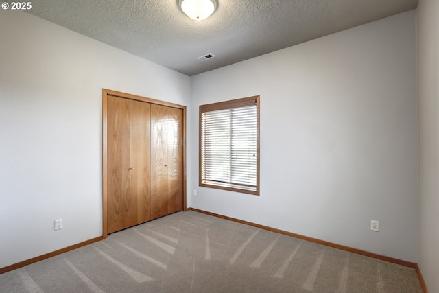 unfurnished bedroom with carpet, visible vents, baseboards, a closet, and a textured ceiling