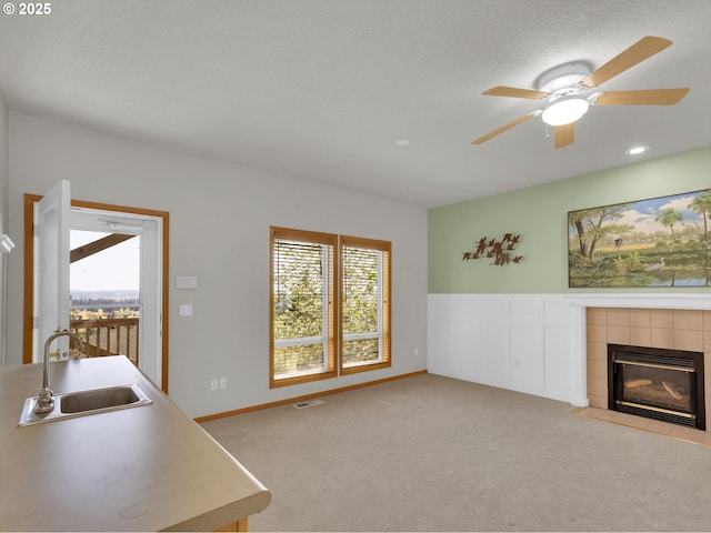 living area with ceiling fan, light colored carpet, a tiled fireplace, baseboards, and visible vents