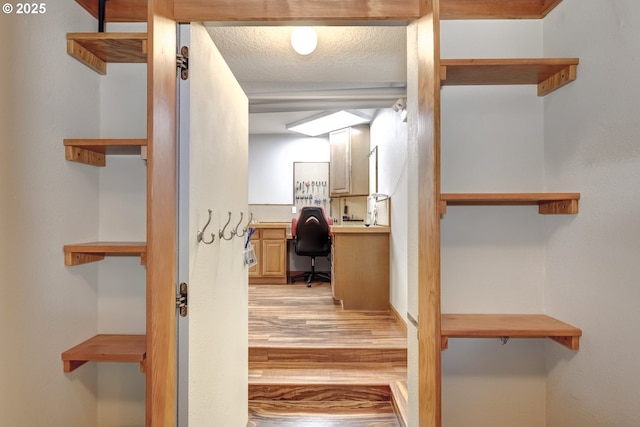 interior space with light wood-type flooring, a textured ceiling, and built in desk