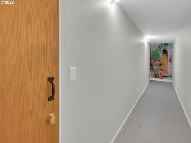 hallway featuring baseboards and finished concrete flooring