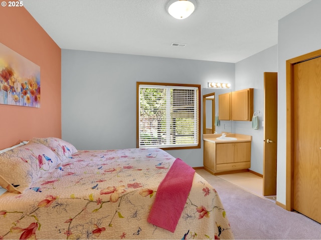 bedroom featuring visible vents, light colored carpet, a sink, baseboards, and ensuite bathroom
