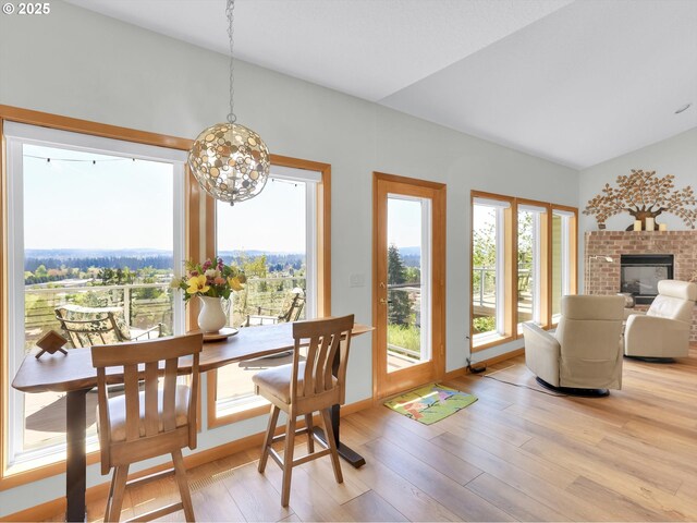 dining area featuring a brick fireplace, a notable chandelier, lofted ceiling, and light wood-style floors