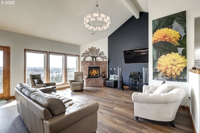 living area featuring beam ceiling, high vaulted ceiling, wood finished floors, an inviting chandelier, and a brick fireplace