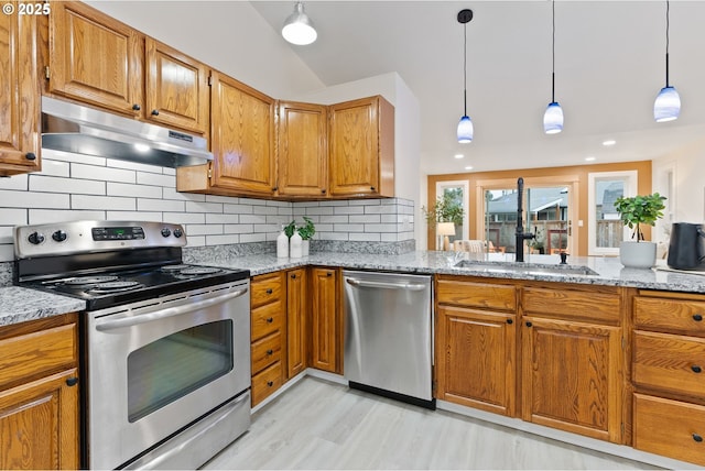 kitchen featuring tasteful backsplash, light stone countertops, under cabinet range hood, brown cabinets, and appliances with stainless steel finishes