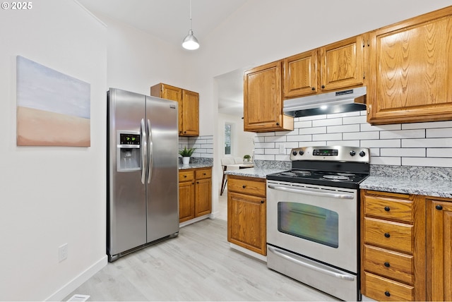 kitchen featuring light stone countertops, brown cabinetry, stainless steel appliances, decorative backsplash, and under cabinet range hood