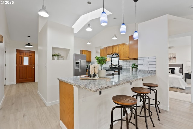 kitchen with light wood-type flooring, brown cabinets, backsplash, stainless steel appliances, and a peninsula