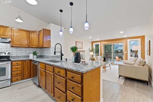 kitchen featuring brown cabinetry, a peninsula, a sink, under cabinet range hood, and appliances with stainless steel finishes