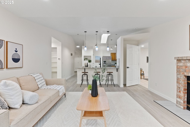 living room featuring light wood-style flooring, a brick fireplace, a skylight, and baseboards