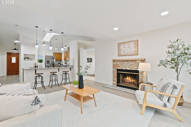 living area with recessed lighting, baseboards, a brick fireplace, and light wood-style flooring