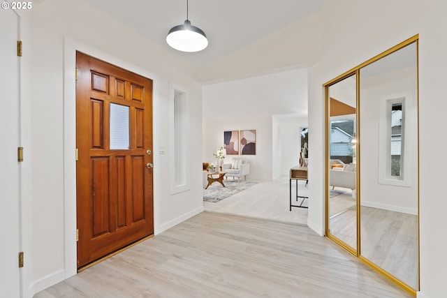 foyer with vaulted ceiling, light wood-style floors, and baseboards