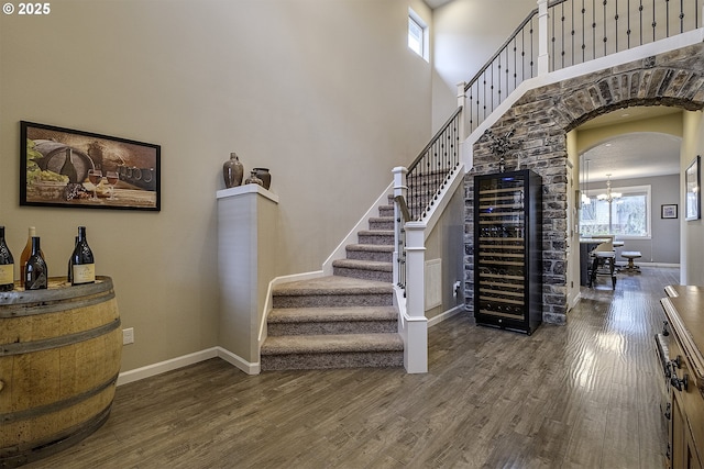 staircase with wood finished floors, beverage cooler, baseboards, a high ceiling, and arched walkways