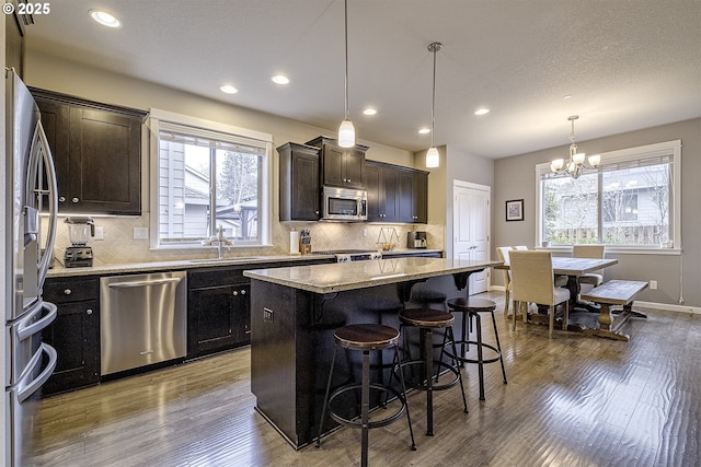 kitchen with a kitchen bar, wood finished floors, appliances with stainless steel finishes, and a kitchen island