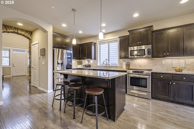 kitchen with tasteful backsplash, dark brown cabinetry, light wood-type flooring, a kitchen bar, and appliances with stainless steel finishes