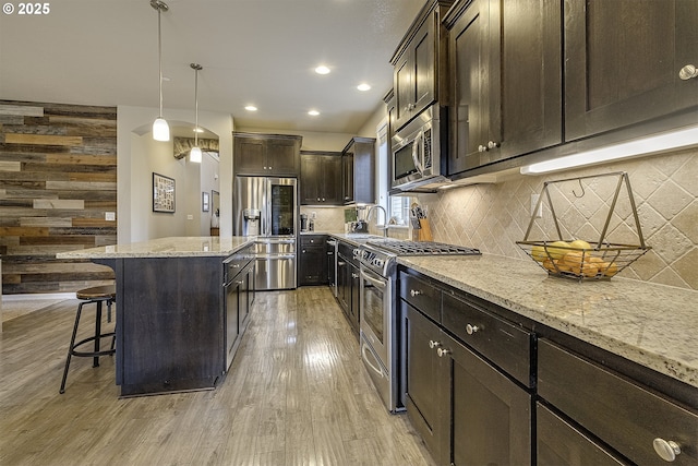 kitchen with light wood finished floors, wooden walls, a breakfast bar, decorative backsplash, and appliances with stainless steel finishes