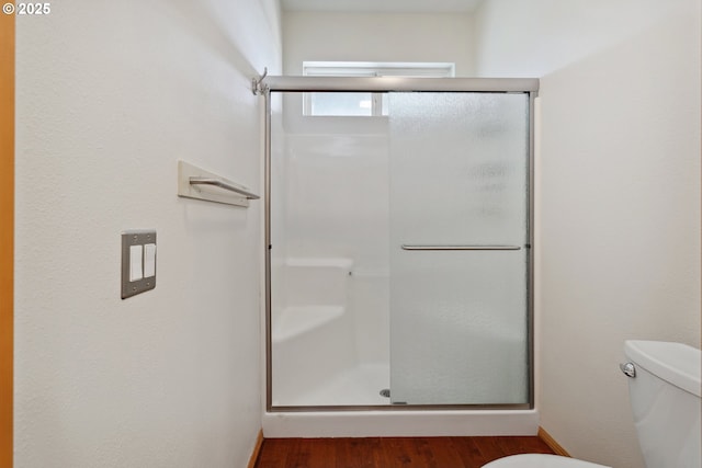 full bath featuring toilet, a stall shower, and wood finished floors