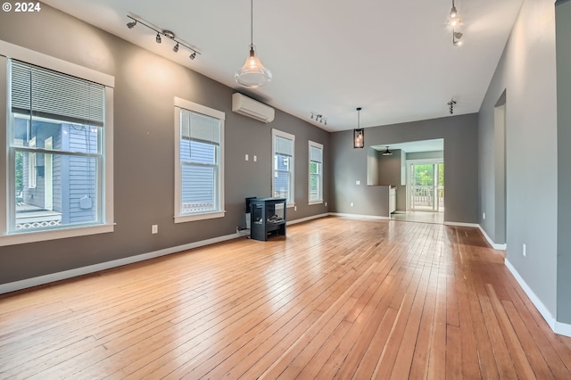 9116 N Willamette Blvd, Portland, OR 97203 - unfurnished living room featuring a wall mounted air conditioner, a wood stove, rail lighting, and light wood-style flooring