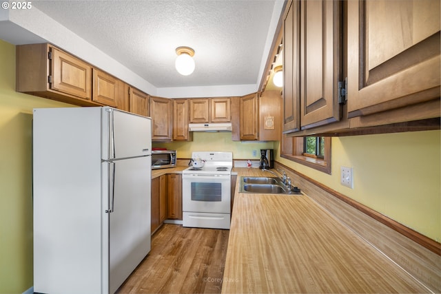 kitchen featuring white appliances, under cabinet range hood, a sink, wood finished floors, and brown cabinetry