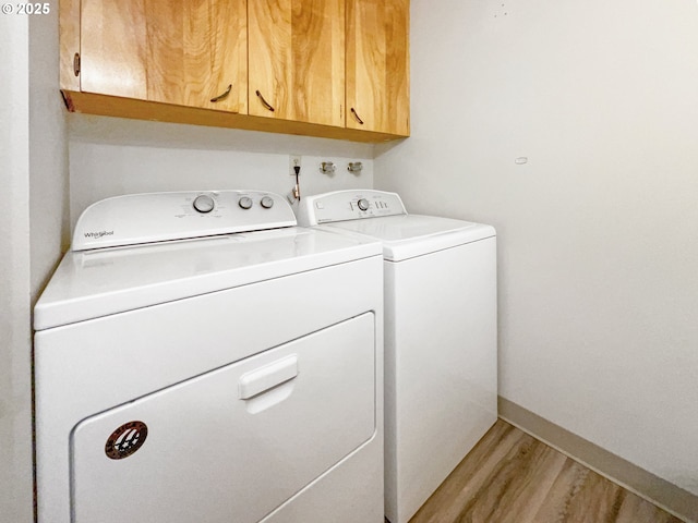 washroom featuring cabinets, washing machine and clothes dryer, and light wood-type flooring