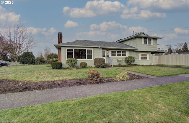 split level home with a front yard, fence, roof with shingles, and a chimney