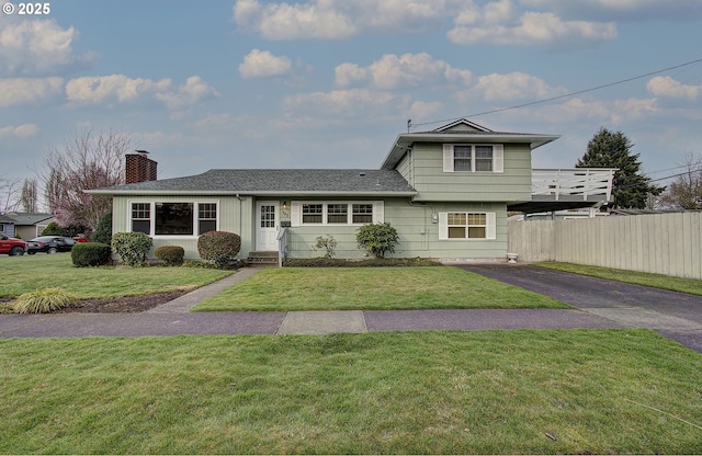 split level home with aphalt driveway, a chimney, a front yard, and fence