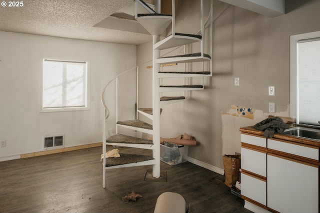 staircase featuring visible vents, a textured ceiling, baseboards, and wood finished floors