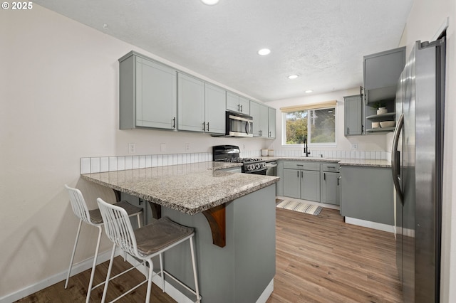 kitchen with kitchen peninsula, appliances with stainless steel finishes, light stone countertops, sink, and hardwood / wood-style flooring