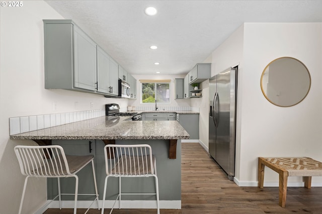 kitchen with kitchen peninsula, a breakfast bar, stainless steel appliances, gray cabinets, and dark hardwood / wood-style floors