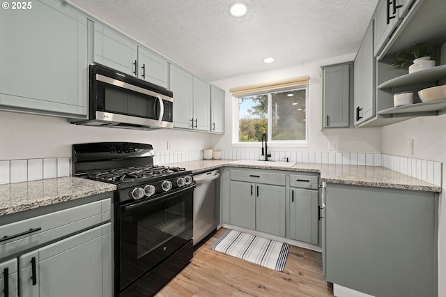 kitchen with light stone countertops, sink, stainless steel appliances, and light hardwood / wood-style flooring