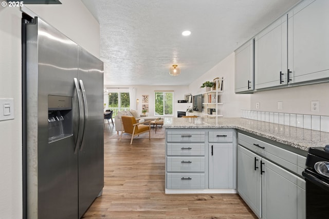 kitchen with light stone countertops, light hardwood / wood-style flooring, kitchen peninsula, stainless steel fridge, and a textured ceiling