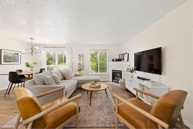 living room with a textured ceiling, a notable chandelier, and light wood-type flooring