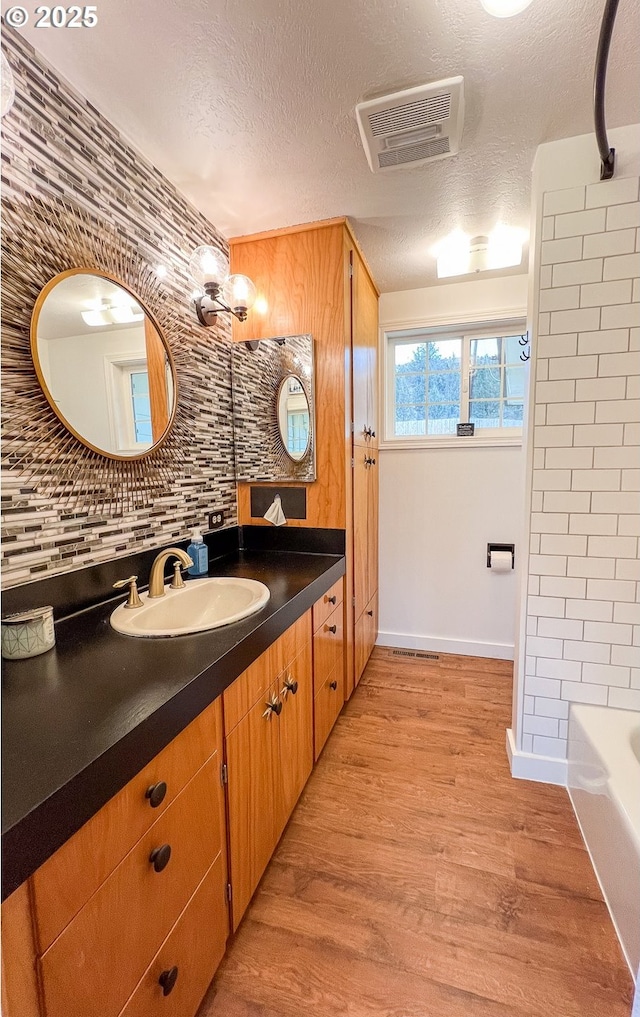 bathroom featuring wood finished floors, a textured ceiling, vanity, backsplash, and baseboards