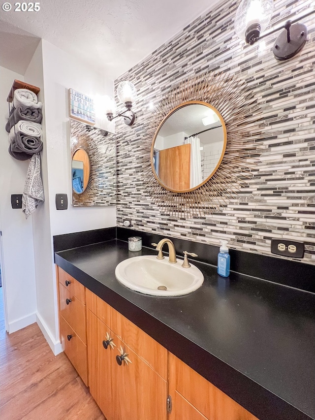 full bathroom featuring wood finished floors, vanity, baseboards, and decorative backsplash