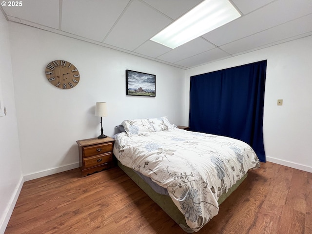 bedroom with a paneled ceiling, wood finished floors, and baseboards