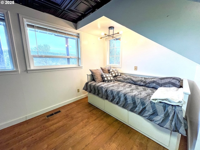 bedroom with baseboards, wood finished floors, visible vents, and an inviting chandelier