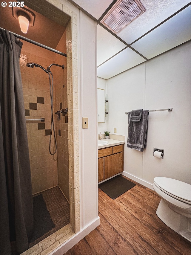 bathroom with wood finished floors, vanity, toilet, and tiled shower