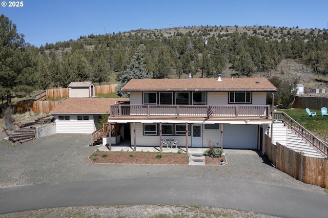 view of front of house with stairway, a view of trees, driveway, and a storage unit