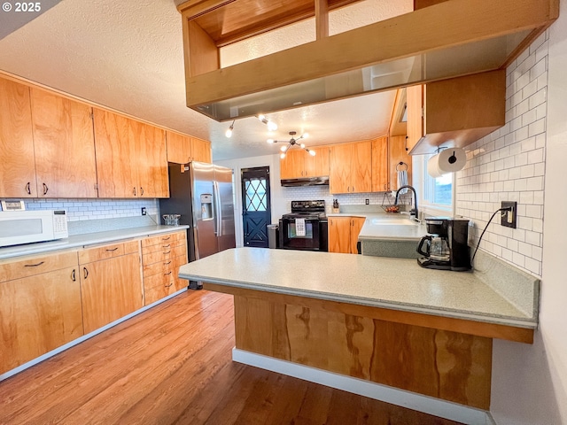 kitchen with backsplash, a sink, white microwave, stainless steel fridge, and black electric range oven