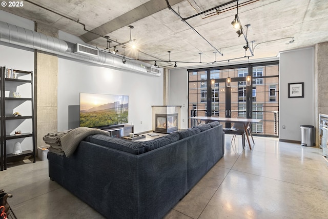 living room featuring a multi sided fireplace, rail lighting, and concrete floors