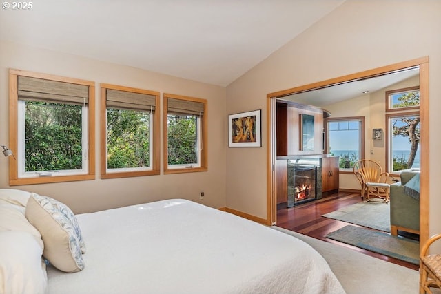 bedroom with lofted ceiling, wood finished floors, baseboards, and a lit fireplace