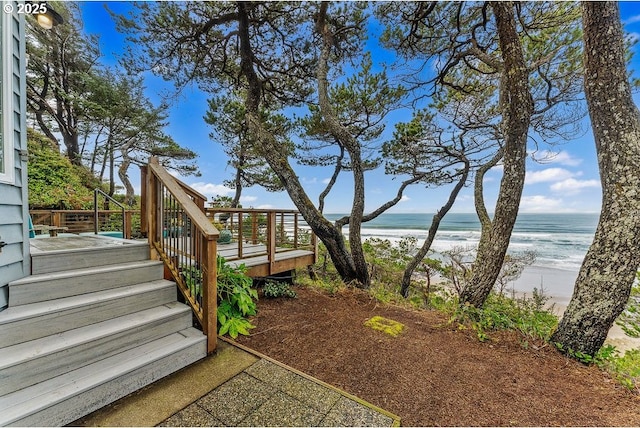 view of yard with a deck with water view and a beach view