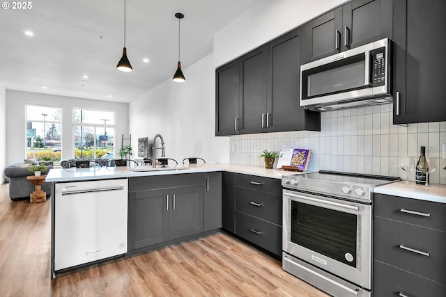 kitchen with kitchen peninsula, appliances with stainless steel finishes, sink, pendant lighting, and light hardwood / wood-style floors