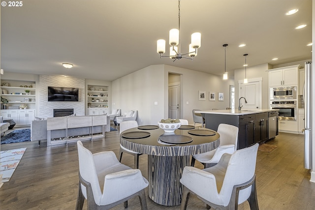 dining room featuring sink, dark hardwood / wood-style flooring, built in features, a notable chandelier, and a fireplace