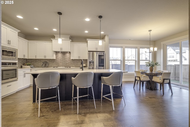 kitchen featuring white cabinetry, appliances with stainless steel finishes, an island with sink, and pendant lighting