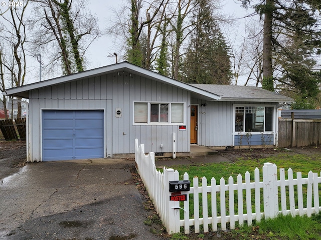 single story home with a fenced front yard, a garage, board and batten siding, and aphalt driveway