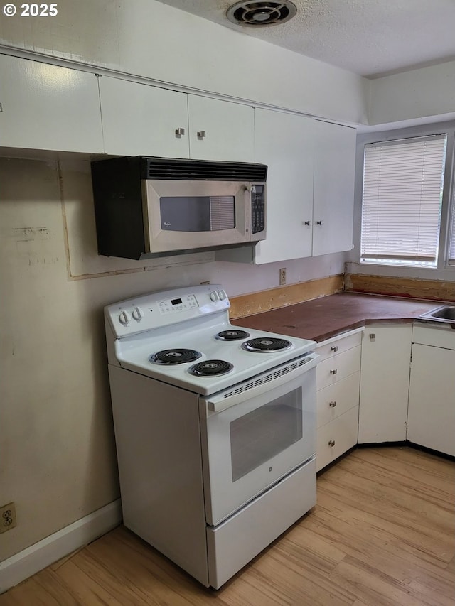 kitchen featuring light wood-type flooring, stainless steel microwave, a textured ceiling, white electric range oven, and white cabinetry