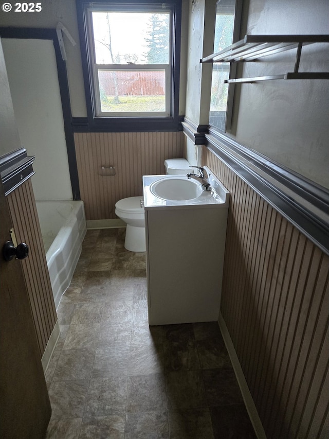 full bath with toilet, wooden walls, wainscoting, a bathtub, and vanity