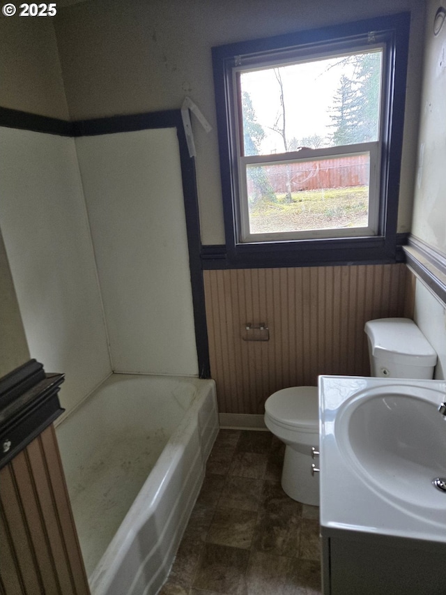 bathroom featuring wooden walls, toilet, a bath, and wainscoting