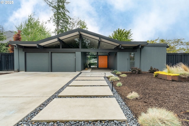 mid-century inspired home featuring fence, an attached garage, and driveway